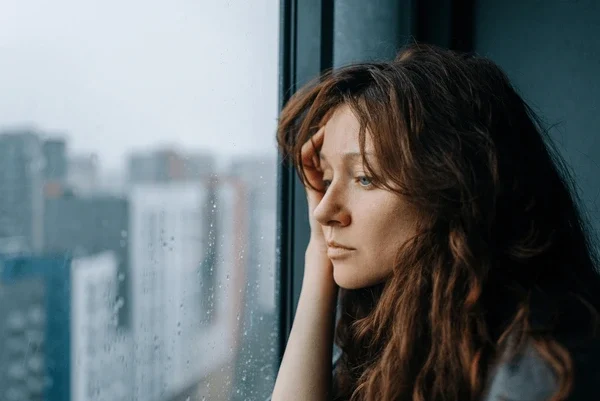 A woman looking sadly out of a rain-covered window, representing depression and anxiety that psychotherapy can help with in Horsham